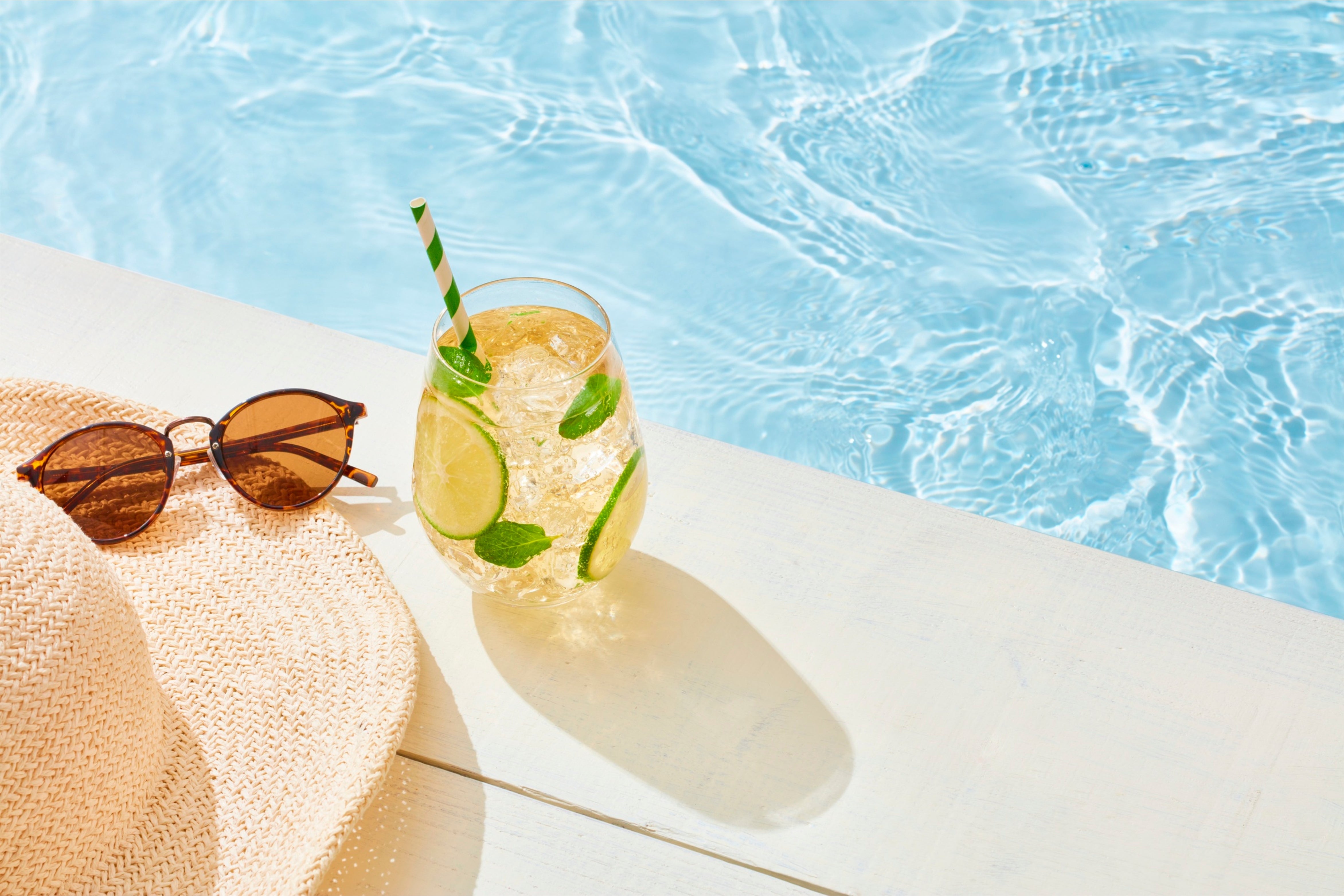 Summer pic of a poolside with a summer hat, sunglasses and a cooling peppermint lemon drink